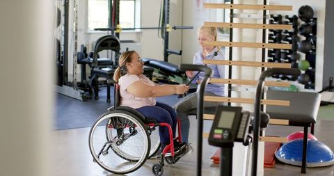 Woman in Wheelchair Undergoing Physio Session with Therapist at Gym
