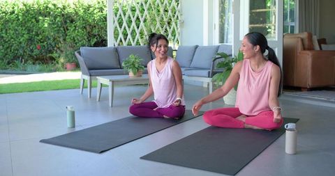 Two women practicing outdoor yoga on patio smiling during morning meditation session