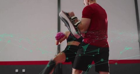 Coach holding kick pad instructing female athlete performing high kick in gym