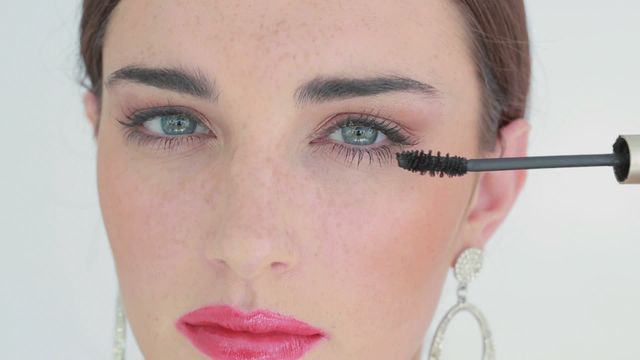 Close-up of woman's face with pink lips while applying mascara on eyelashes. Perfect for beauty tutorials, makeup product advertisements, fashion magazines, skincare promotions, and cosmetics blogs. Ideal for showing makeup application techniques and detailed eye makeup looks.