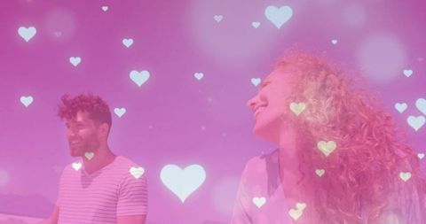 Laughing couple standing on shoreline with pink heart bokeh overlay