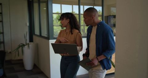 African american coworkers walking and talking with laptop and tablet in modern office