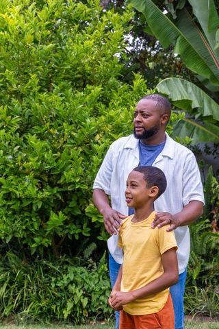 African american father and son standing in lush backyard placing hands on shoulders
