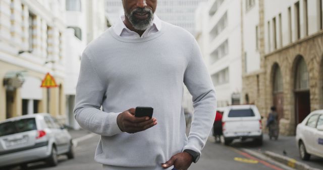 Man Wearing Casual Clothes Walking Down Urban Street While Looking at Mobile Phone - Download Free Stock Images Pikwizard.com