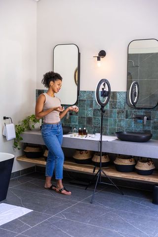Filming skincare tutorial in modern bathroom with ring light, vanity, and teal tile