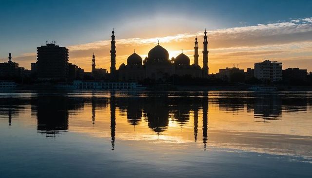 Golden sunset silhouette mosque with minarets and river reflections, riverside skyline