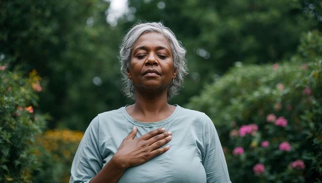 Older woman practicing mindful breathing with hand over heart in lush garden retreat serene