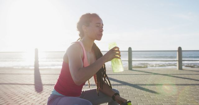 African american woman exericisng drinking water on promenade by the sea. fitness healthy outdoor urban lifestyle.