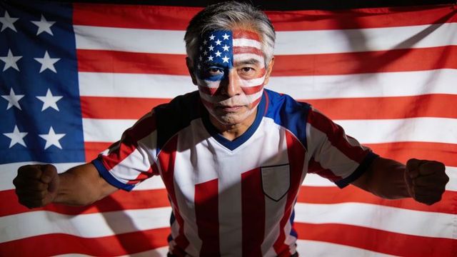 Gray-haired man wearing american flag face paint and jersey raising fists in patriotic portrait