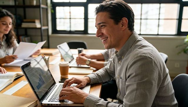 Smiling professional typing on laptop during collaborative office meeting, modern coworking