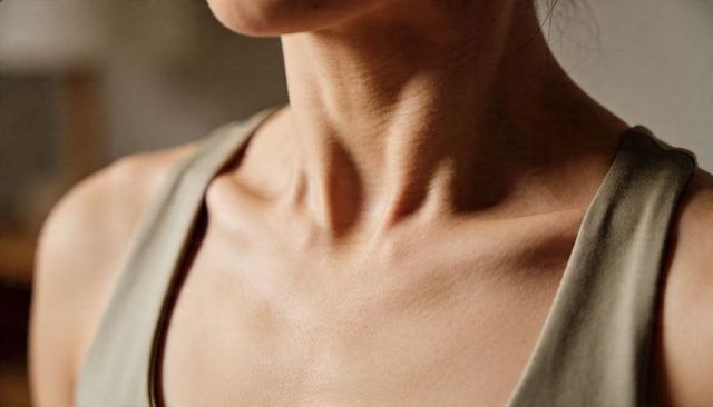 Close-up female neck and collarbone in olive tank showing healthy glowing skin and warmth