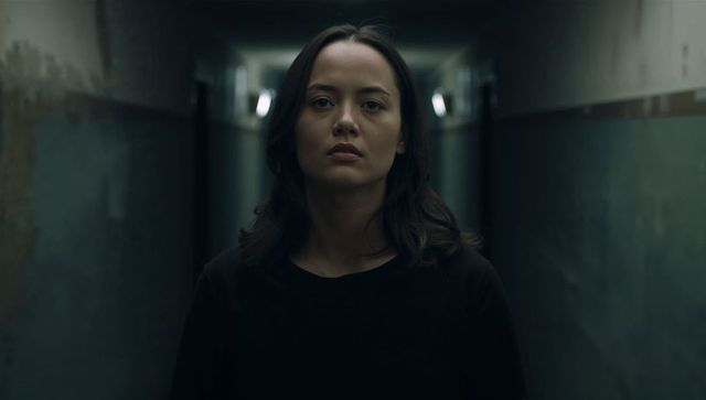 Woman standing in narrow dim corridor wearing black top waiting moody gritty portrait