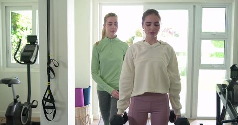Home gym partners training with dumbbells and spotting support in bright natural light