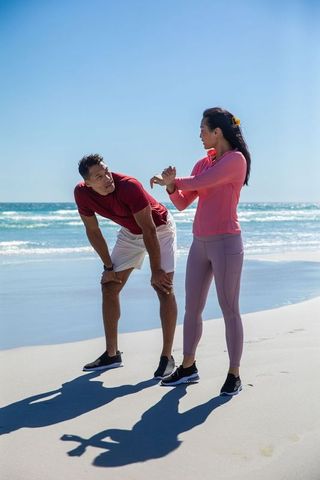 Fitness Partners Stretching by Ocean at Beach