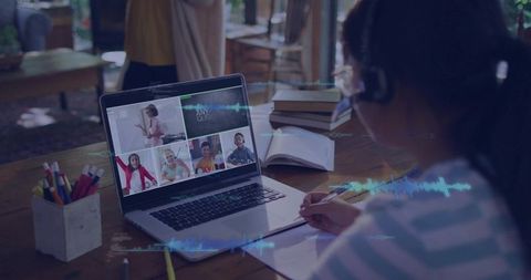 Child writing in notebook during virtual classroom session with laptop and headphones