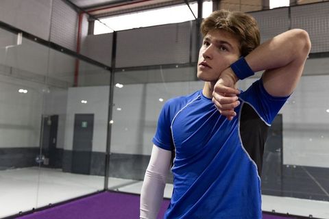Young male athlete cooling down on indoor glass court in blue training top
