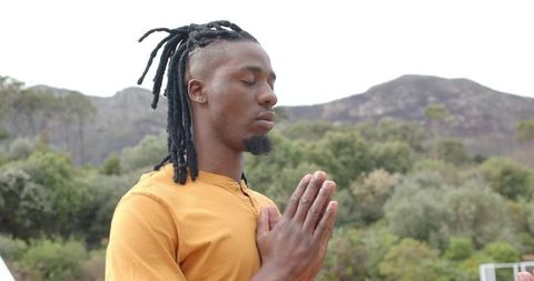 African american man practicing meditation outdoors with hands in prayer pose amid mountains