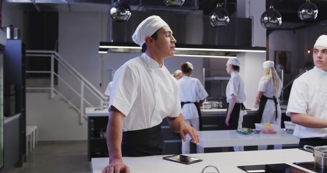 Professional chefs dressed in white uniforms collaborate in a sleek, modern kitchen environment. Ideal for use in content related to culinary training, professional cooking environments, teamwork in kitchens, or modern gastronomy techniques. Depicts a scene where new recipes and ideas are being discussed and developed.