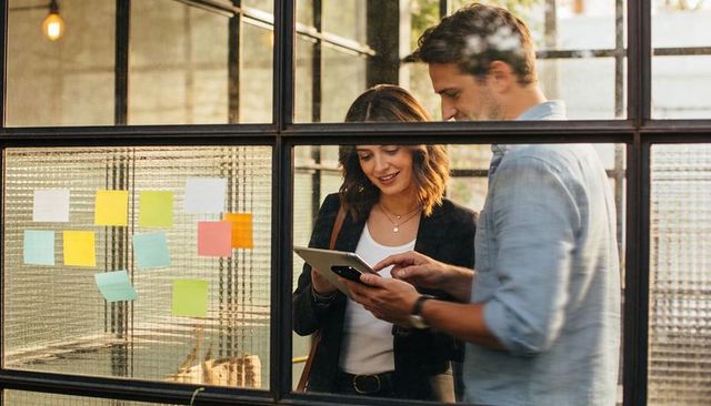 Two colleagues reviewing tablet and collaborating in modern office with sticky notes