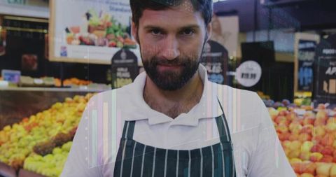 Confident grocery clerk wearing striped apron standing among fresh apples and produce