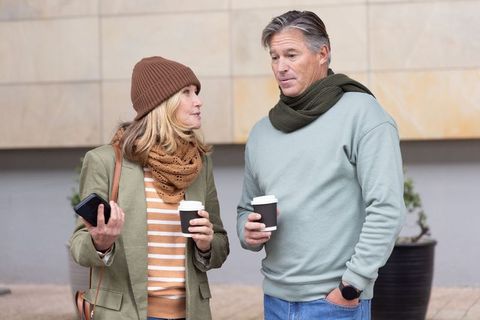 Middle-aged couple chatting while holding takeaway coffee outdoors in urban winter attire