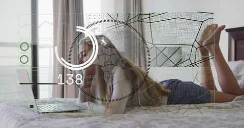 Young woman lying on bed checking laptop with futuristic hud overlay in sunlit bedroom
