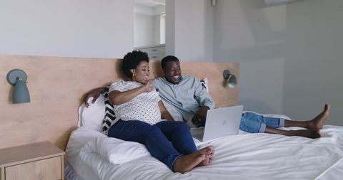 African American couple relaxing on bed using laptop in modern minimalist bedroom