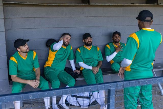 Baseball team discussing strategy in dugout wearing green and yellow uniforms