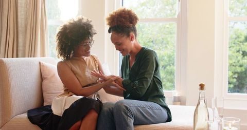 Mid-adult African American women sharing intimate moment examining hands on cozy sofa