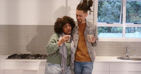 Cozy couple leaning in modern kitchen holding mugs embracing morning togetherness