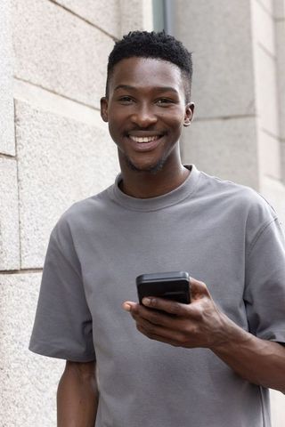 Young man smiling while using smartphone on urban sidewalk
