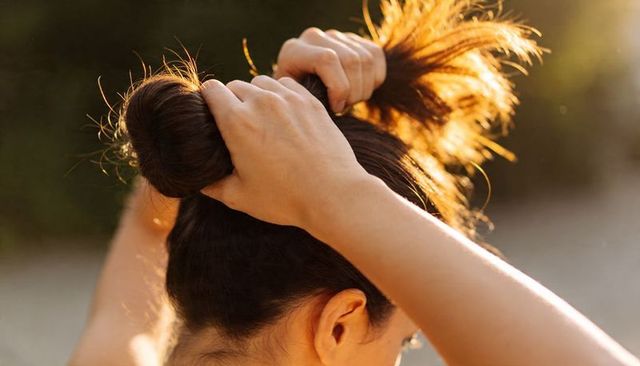 Young woman tying hair into bun backlit by golden hour sun outdoors close-up hands