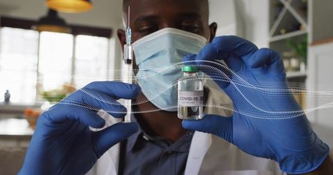 Clinician preparing covid-19 vaccine vial and syringe wearing mask and blue gloves
