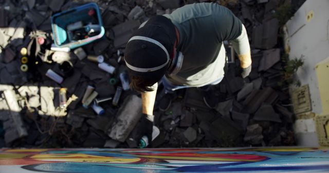Artist is seen spray painting vibrant graffiti on an urban wall. The image showcases the process of creating street art, with various spray paint cans and tools around. Useful for illustrating topics related to urban culture, creativity, and artistic expression.