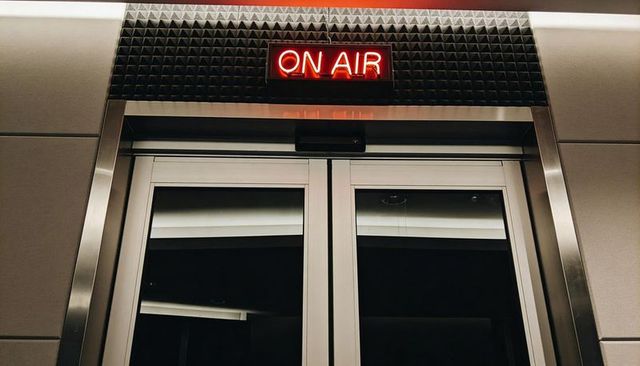 Neon on air sign glowing above double glass doors with acoustic foam and metal trim