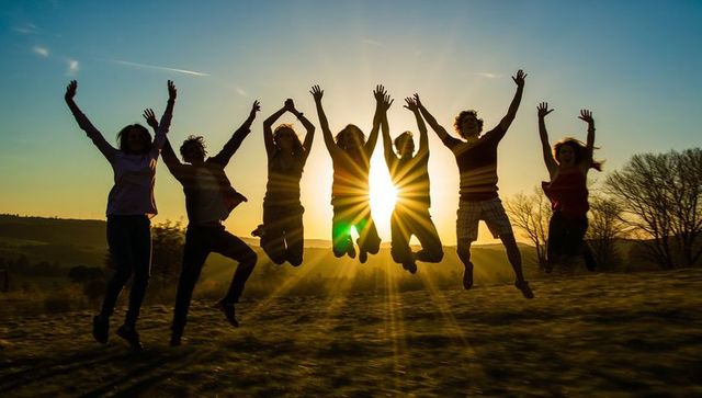Friends jumping at sunset with dramatic sunburst silhouettes celebrating joy and freedom