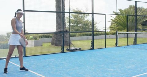 Woman playing padel on blue court swinging racket near palm trees