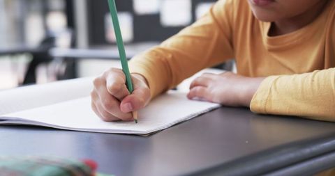 Focused Student Writing in Classroom with Yellow Shirt and Green Pencil - Download Free Stock Images Pikwizard.com