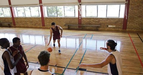 Adult basketball player dribbling across gym hardwood court during fast-break play