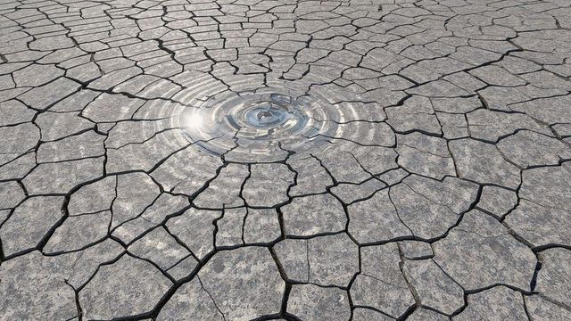 Water ripple on cracked dry lake bed under bright sun