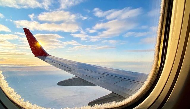Sunrise over wingtip through frosted cabin window capturing in-flight sky and horizon