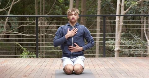 Young man practicing mindful breathing outdoors on yoga deck