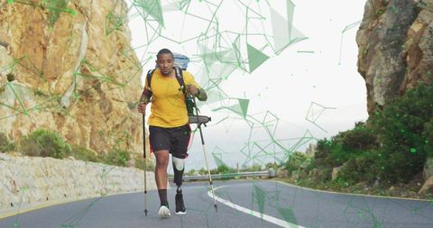 Determined amputee athlete running uphill on winding mountain road with poles and backpack