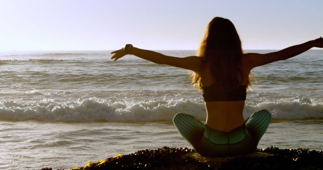 Back view of caucasian woman in sport outfit practising yoga on beach at sunrise. Lifestyle, fitness, wellbeing, yoga and meditation, unaltered.
