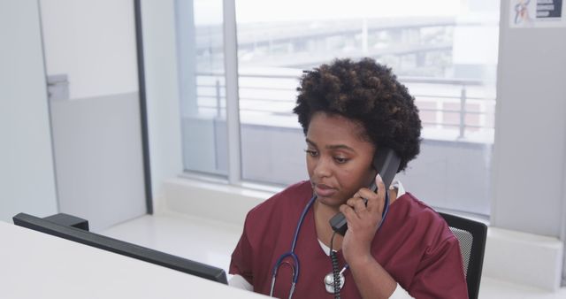 Focused African American Nurse Using Phone and Computer at Hospital Desk - Download Free Stock Images Pikwizard.com