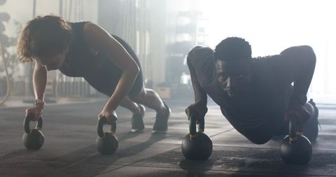 Diverse young adults holding plank on kettlebells at gym