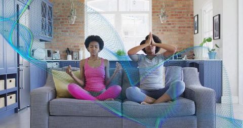 Mother and daughter meditating together on grey sofa in sunlit open-plan kitchen