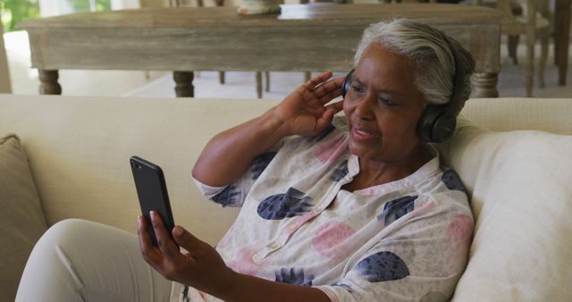 Smiling african american senior woman wearing headphones having a image call on smartphone at home. retirement senior lifestyle living concept