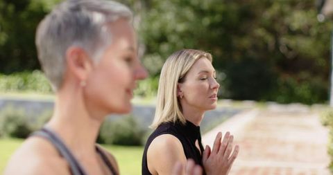 Two women meditating in sunlit garden practicing mindfulness and holistic wellness