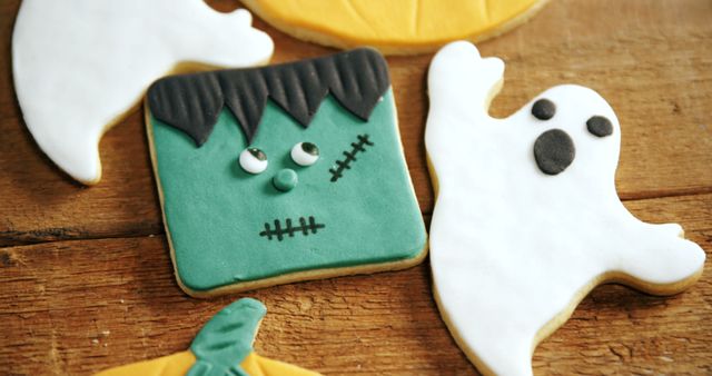 Colorful Halloween-themed cookies on wooden surface, featuring Frankenstein's monster, a ghost, and a pumpkin. Ideal for Halloween party decorations, children's celebrations, fall-themed social media posts, festive baking advertisements, and cookbooks.